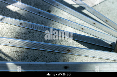 Chiudere fino ad alto angolo di visione di una serie di passi concreti con protezione di bande metalliche in corrispondenza dei bordi di andare verso il basso in un trimestre a spirale, sotto le ombre e la mattina Foto Stock