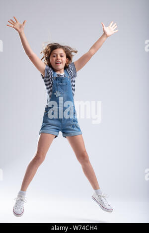 Athletic snello giovane ragazza di saltare in aria con le braccia tese e le gambe e un sorriso su uno sfondo bianco Foto Stock