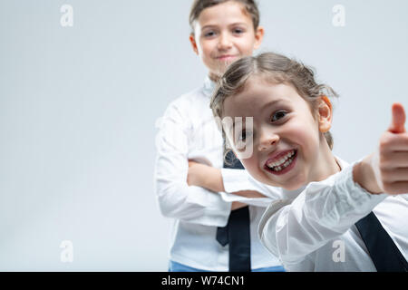 Cheeky poco entusiasta ragazza dando un pollice in alto con un raggiante sorriso guardato da dietro da lei sorridente sorella Foto Stock