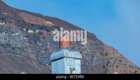 Un vecchio camino isolata contro una montagna e nitido cielo blu immagine di sfondo in formato paesaggio con spazio di copia Foto Stock