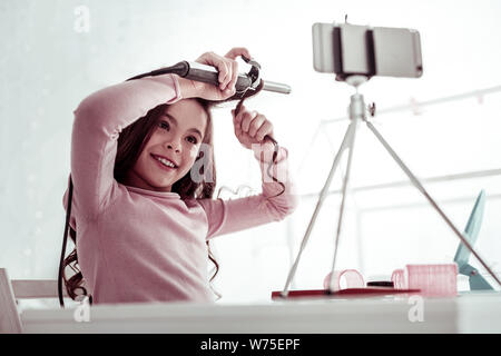 Gioiosa bella ragazza utilizzando un professionista di ferro arricciacapelli Foto Stock