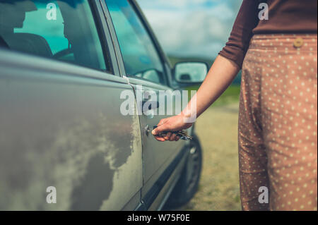 Una giovane donna di sbloccaggio è la sua auto in natura in un giorno di estate Foto Stock