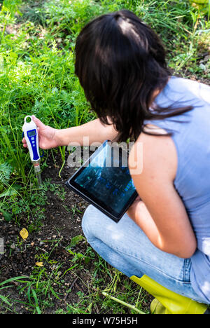 Misuratore di PH tester nel suolo. Misurare suolo con il dispositivo digitale e tablet. Donna agricoltore in un giardino. Concetto per la nuova tecnologia nel settore dell'agricoltura. Foto Stock