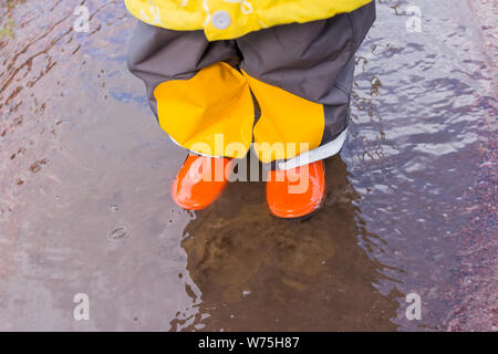 Le gambe del bambino in arancione stivali di gomma che si tuffa in autunno pozzanghere. bambini luminose stivali di gomma,giardinaggio. Rainy day fashion.Giardino piovosa scarpe di gomma Foto Stock