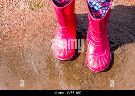 Le gambe del bambino in arancione stivali di gomma che si tuffa in autunno pozzanghere. bambini luminose stivali di gomma,giardinaggio. Rainy day fashion.Giardino piovosa scarpe di gomma Foto Stock