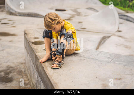 Ragazzo mette in ginocchio pastiglie e fasce da braccio prima formazione skateboard Foto Stock