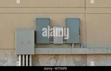 Grigio metallo box utility attaccata alla parete esterna di un edificio con dei cavi elettrici che li collega. Foto Stock