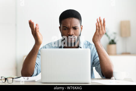 Sottolineato AFRICAN-AMERICAN businessman guardando lo schermo del notebook in ufficio moderno Foto Stock