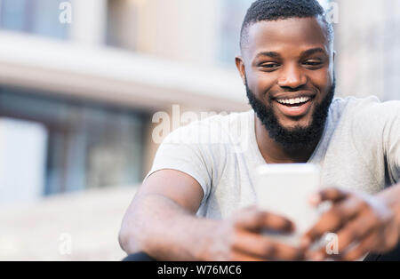 Bello l'uomo africano rendendo selfie e sorridente outdoor Foto Stock