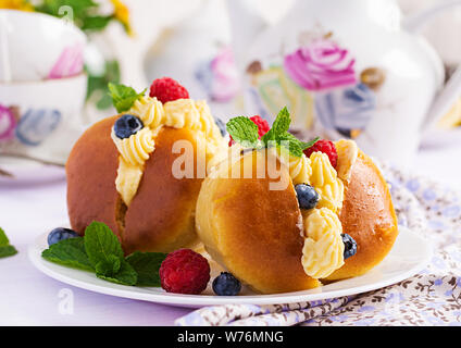 Il Rum baba decorate con panna montata e fresca lampone, mirtillo. Savarin al rum, crema e frutti di bosco. Cucina italiana Foto Stock