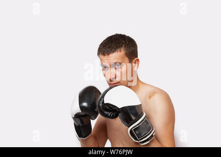 Un uomo in guanti da boxe con ammaccature sul suo corpo e viso sorge in un rack durante una lotta e pugilato su un bianco sfondo isolato Foto Stock