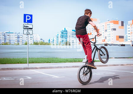 Teenage biciclette BMX Rider in un parcheggio con Auto Blu Parcheggio Accesso Disabili Parcheggio Disabili segno. Extreme BMX Freestyle bicicletta in prossimo Foto Stock