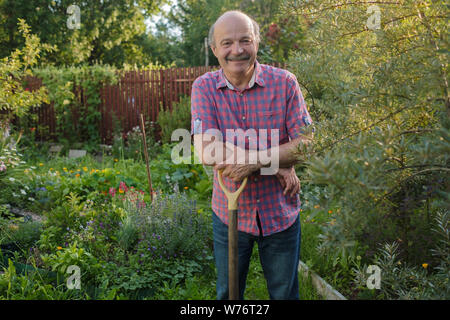 Uomo anziano con un baffi in piedi nel giardino estivo, sorridente. Foto Stock