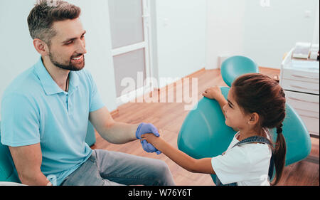 Dentista agitando la mano per il suo piccolo paziente. Bambina visitando dental clinic. Odontoiatria Pediatrica Foto Stock