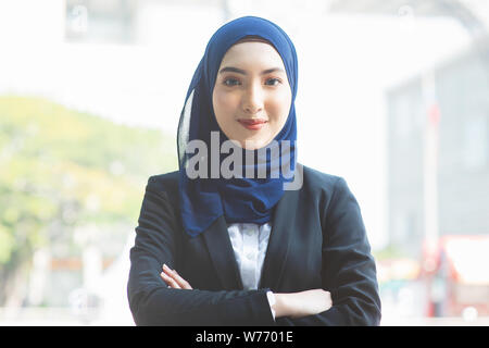 Ritratto di donna musulmana in business suit, con le braccia incrociate e sorriso guardando la fotocamera. Foto Stock