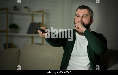 Annoiato uomo canali di commutazione sul TV e sbadigli Foto Stock