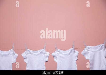 Bianco corpo baby suit appeso da una linea contro un sfondo rosa Foto Stock