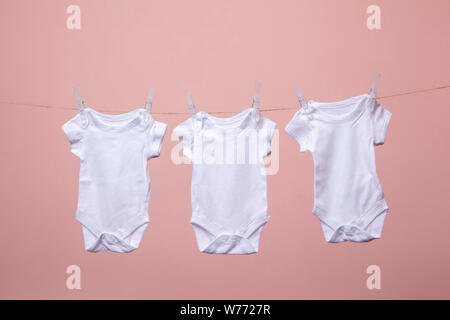 Bianco corpo baby suit appeso da una linea contro un sfondo rosa Foto Stock