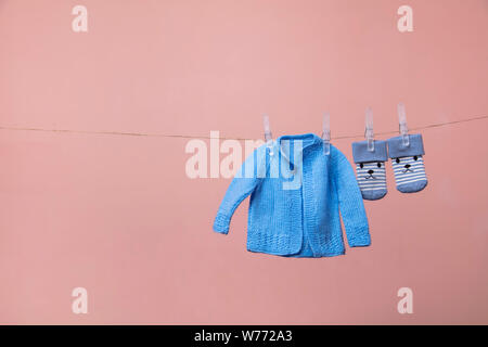 Lavorate a maglia new born baby jumper e calzini appesi su una linea di abbigliamento contro rosa Foto Stock