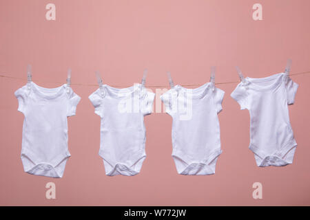 Bianco corpo baby suit appeso da una linea contro un sfondo rosa Foto Stock