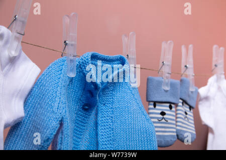 Lavorate a maglia new born baby jumper e calzini appesi su una linea di abbigliamento contro rosa Foto Stock