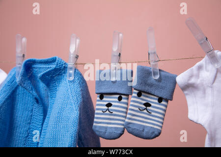 Lavorate a maglia new born baby jumper e calzini appesi su una linea di abbigliamento contro rosa Foto Stock