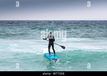 Un stand up paddle boarder voce fuori in mare a Fistral a Newquay in Cornovaglia. Foto Stock