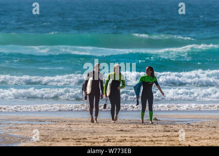 Femmina adolescente surfers che trasportano le loro tavole da surf e camminare al di fuori del mare a Fistral Beach in Newquay in Cornovaglia. Foto Stock