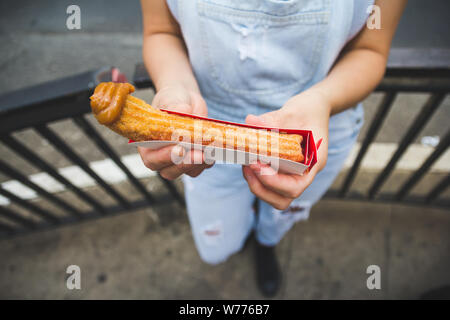 Churro. è un fritto a pasta pasticceria snack. Stile brasiliano con il latte dolce punta. Popolare in paesi come il Portogallo, la Spagna e il Brasile. Giovane donna holding swe Foto Stock