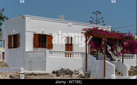 Una casa dipinta di bianco con persiane in legno e bouganville crescente oltre che della veranda cancello in Santorini Foto Stock