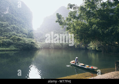 Ninh Binh, Vietnam - Maggio 2019: donna vietnamita in un ceppo di legno barca a remi attraversando Trang un parco della natura. Foto Stock