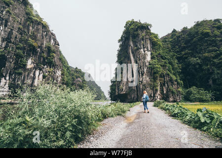 Caucasian donna bionda si affaccia su montagne calcaree a Ninh Binh provincia, Vietnam. Foto Stock