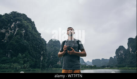 Uomo caucasico con vintage cinepresa nelle sue mani che si affaccia sulle montagne di calcare in Ninh Binh provincia, Vietnam Foto Stock