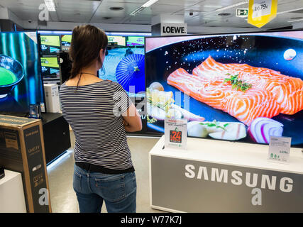 Donna che guarda al nuovo Samsung High definition 4k curva schermi TV in negozio elettrico
