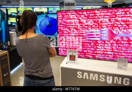 Donna che guarda al nuovo Samsung High definition 4k curva schermi TV in negozio elettrico