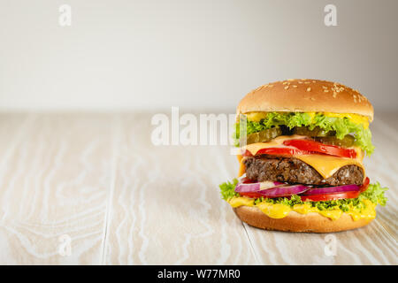 Deliziosi burger con carne, formaggio fuso, gocciolamento e salsa di verdure su legno bianco sfondo rustico con spazio per il testo. Preparata di fresco gustoso prosciutto Foto Stock