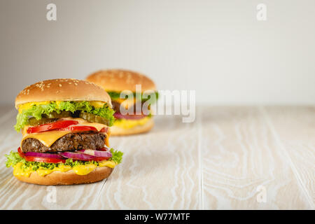 Due deliziosi hamburger con carne, formaggio fuso, gocciolamento e salsa di verdure su legno bianco sfondo rustico con spazio per il testo. Appena sfornati tast Foto Stock