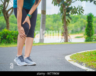 Sport donna che soffre di dolore nella caviglia mentre è seduto sulla strada nel giardino. Foto Stock