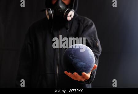 La guerra nucleare minaccia o l'inquinamento globale del concetto. Uomo con maschera a gas azienda globo terrestre in mano uno sfondo scuro. 3d illustrazione Foto Stock