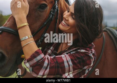 Ritratto di donna bella e cavallo al cavallo fattoria. Cowgirl petting il suo cavallo e sorridente. Foto Stock