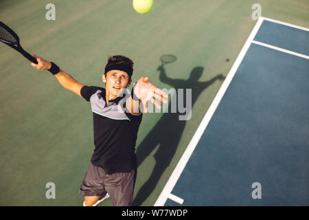 Vista superiore del giovane uomo in abbigliamento sportivo nel lanciare la palla per il servire. Giocatore di tennis che serve la palla in un match. Foto Stock