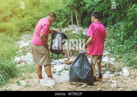 Gli studenti di sesso maschile aiutano a rimuovere i rifiuti dalla classe al mucchio di rifiuti. Messa a fuoco selettiva su nero garbage bag. Foto Stock