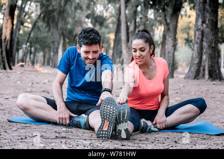 Giovane seduto in un parco a fare esercizi di stretching Foto Stock