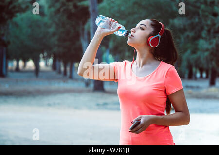 Donna di bere acqua da una bottiglia e ascolta la musica mentre ti alleni Foto Stock