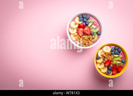 Estate acai smoothie ciotola con fragole, banana, mirtilli, kiwi e granola pastello su sfondo rosa. Tazza colazione con frutta e cere Foto Stock