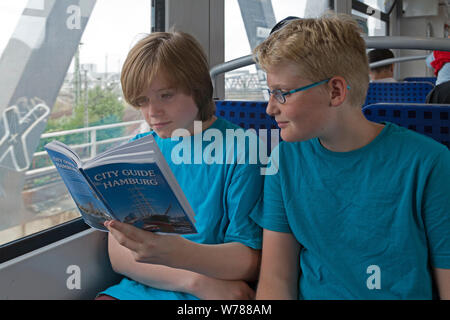 Gli adolescenti durante lo studio della lingua corsa nello studio della loro guida della città su un treno suburbano, Amburgo, Germania Foto Stock