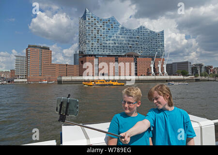 Gli adolescenti durante lo studio della lingua corsa tenendo selfies passando Elbe Philharmonic Hall su un traghetto, Amburgo, Germania Foto Stock