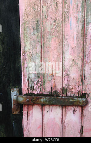 Vecchio garage in legno porta con turbati dalle intemperie di colore rosso o rosa vernice Foto Stock