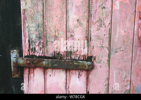 Vecchio garage in legno porta con turbati dalle intemperie di colore rosso o rosa vernice Foto Stock