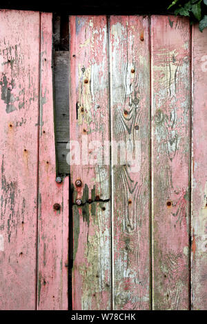 Vecchio garage in legno porta con turbati dalle intemperie di colore rosso o rosa vernice Foto Stock